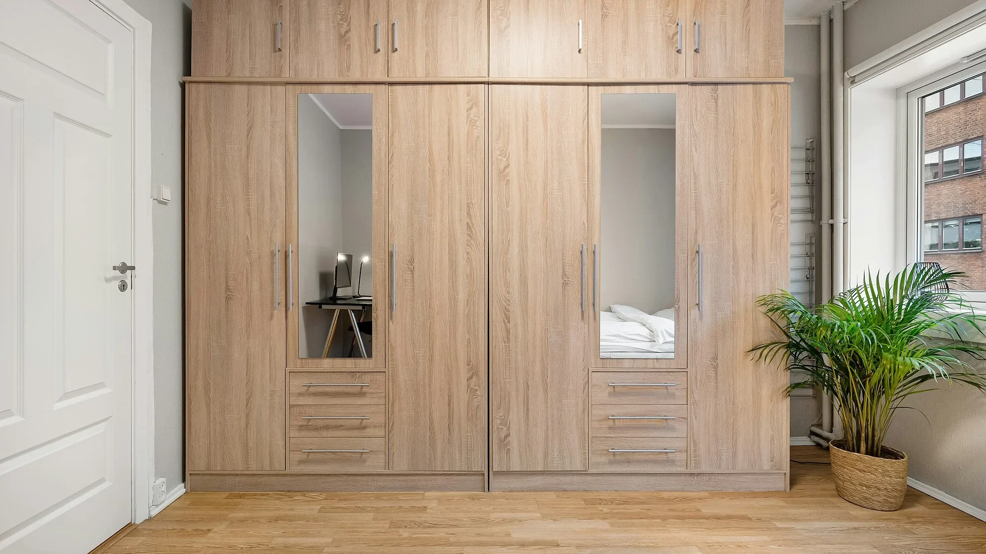 Closet de madera clara empotrado con puertas, espejos y cajones en una recámara